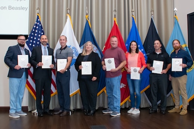 A group of people stand in front of flags holding certificates