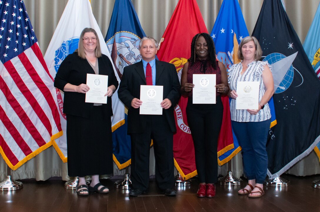A group of people stand in front of flags holding certificates