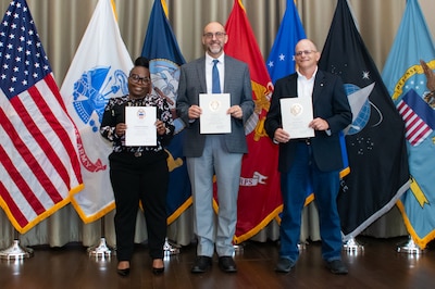 A group of people stand in front of flags holding certificates