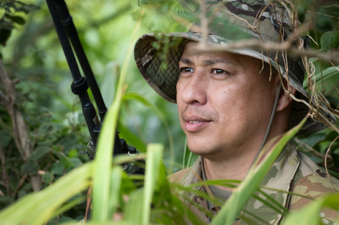 Close-up of service member holding a device in a wooded area.