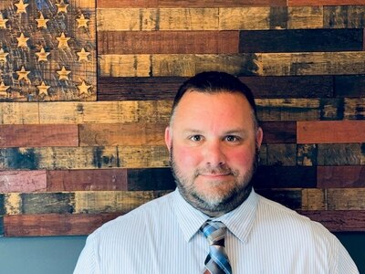 Head and shoulders picture of a white man standing in front of a painted American flag.
