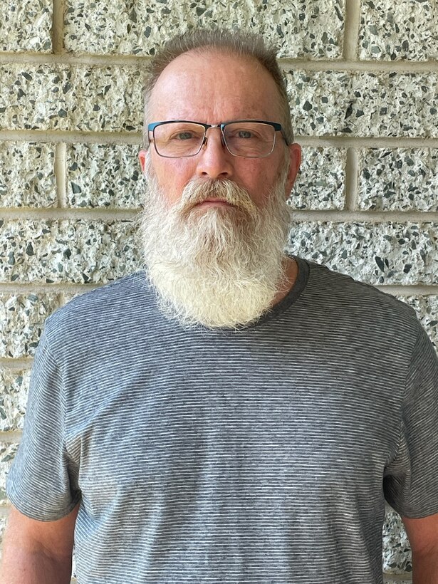 Head and shoulders picture of a white man with a beard standing in front of a brick wall