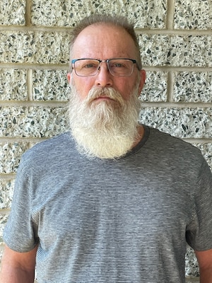 Head and shoulders picture of a white man with a beard standing in front of a brick wall