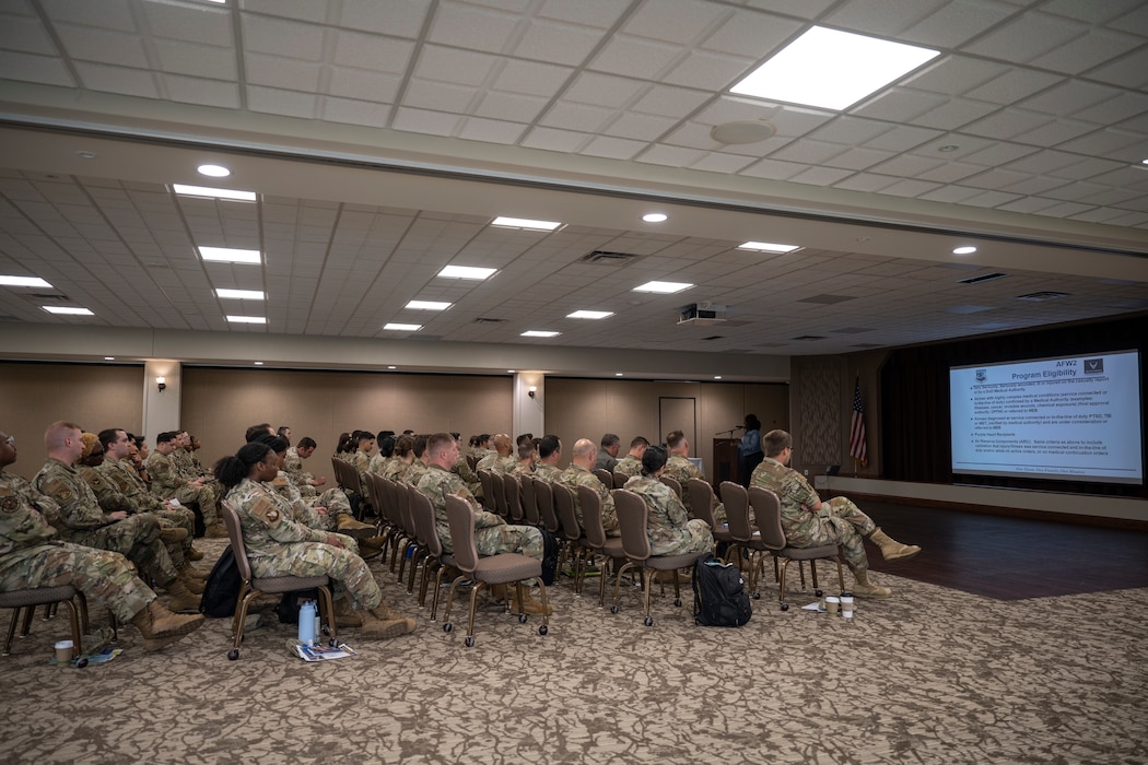 A uniformed service member speaks to civilians during a briefing.