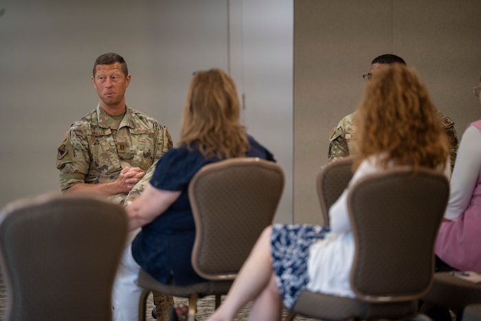 A uniformed service member speaks to civilians during a briefing.