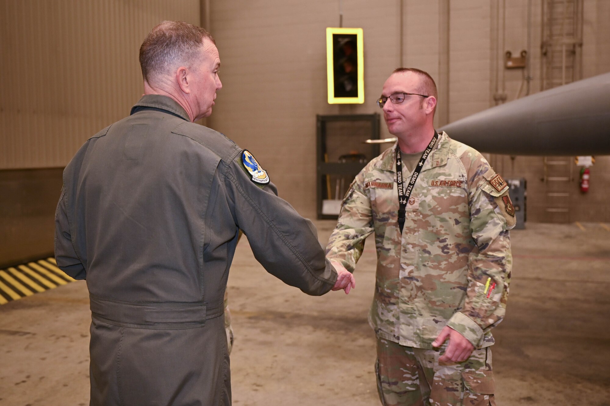 Gen. Guillot hands a coin to an Airman from the 18th Fighter Generation Squadron inside an F-16 hangar.