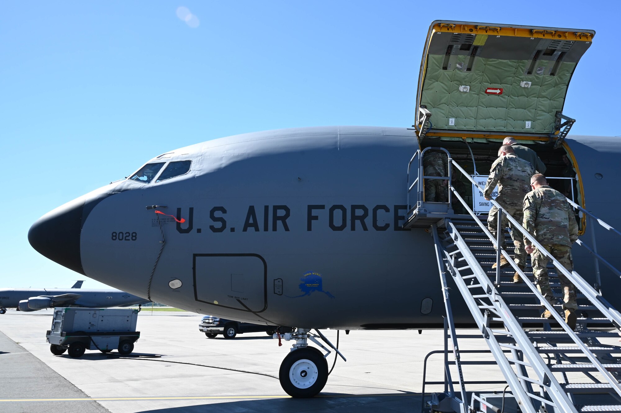 3 Air Force members climb stairs to enter a KC-135 tanker on the flightline.