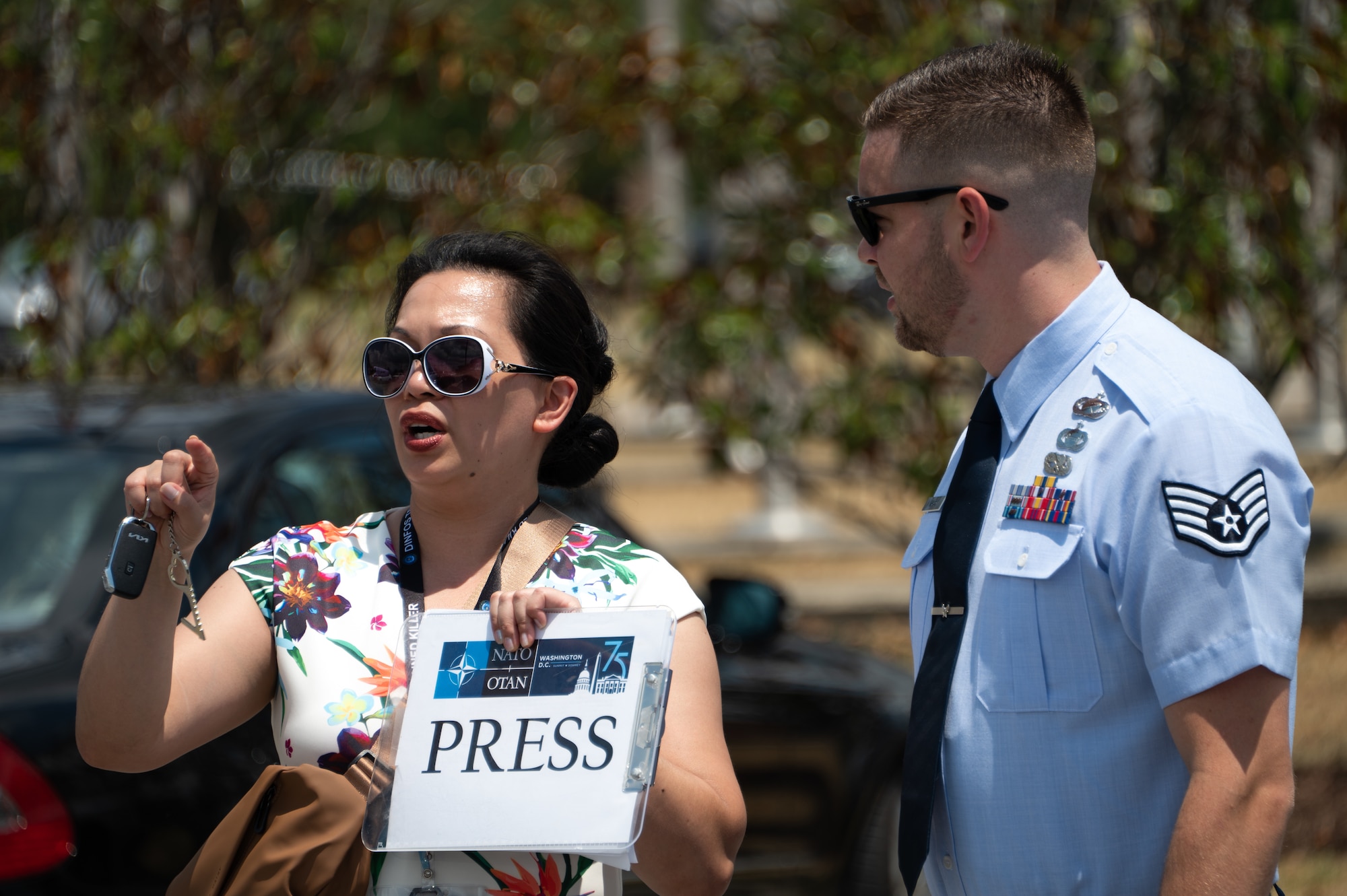 A woman and an U.S. Air Force service member wearing his blue dress uniform stand outside holding a clipboard that says press on it.