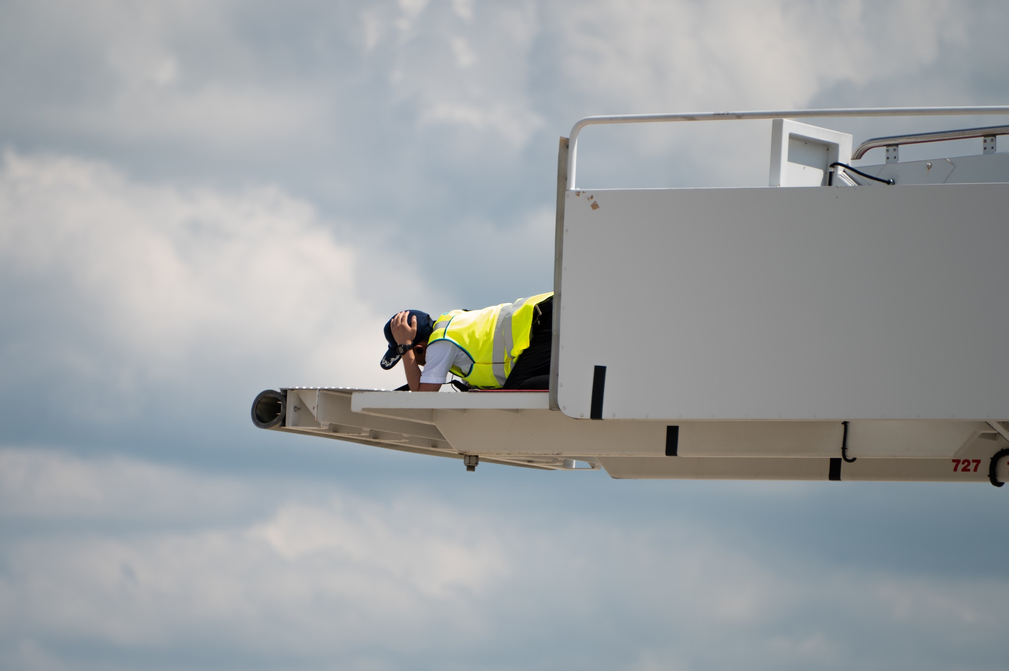 A flightline specialist lays on top of a stair truck with cloudy skies in the distance.