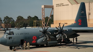 A side profile of parked MAFFS Air Force Reserve C-130 faces away from a giant military hangar as two Air Force Reserve Airmen exit the aircraft.