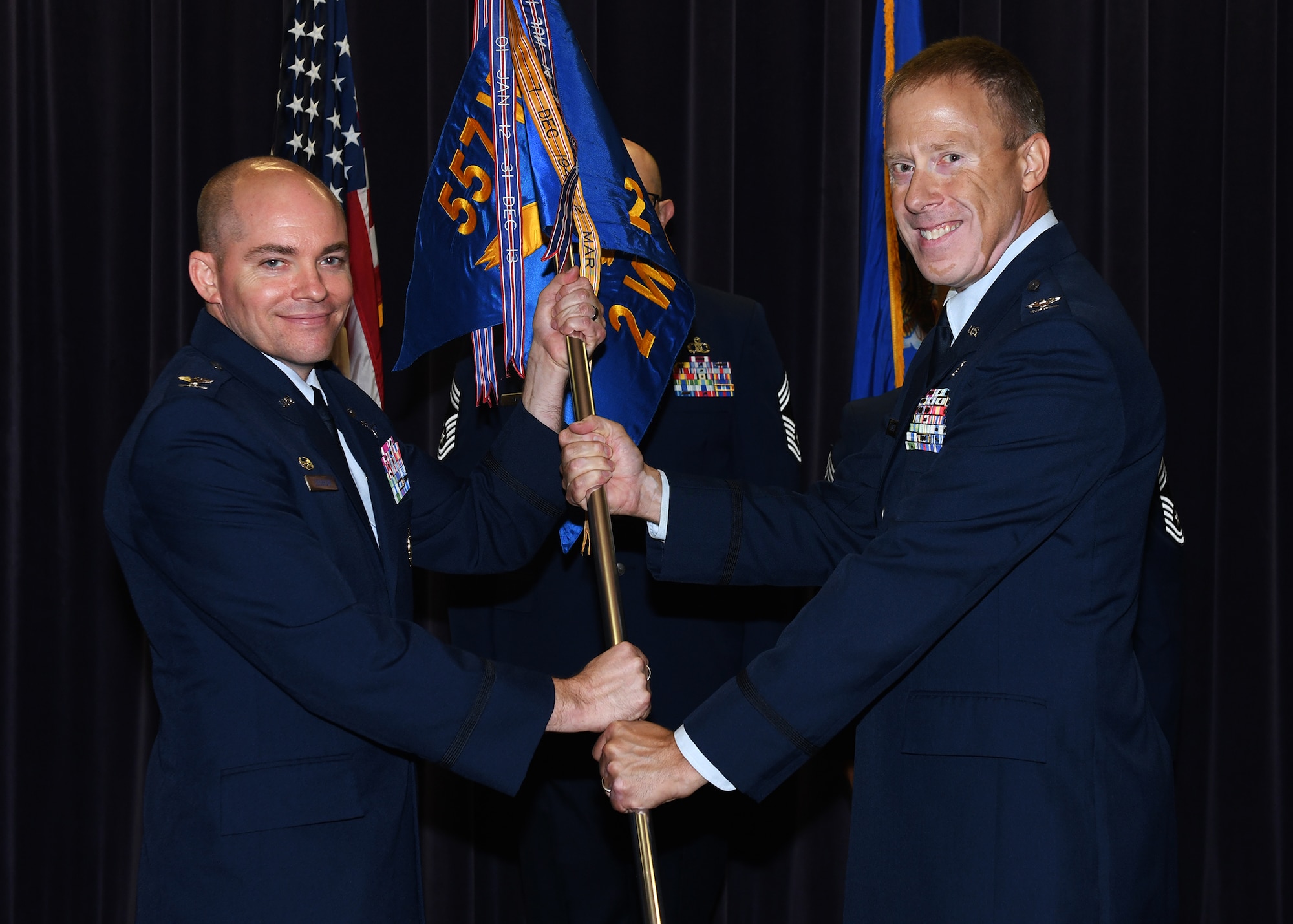 Two Air Force men in uniform passing a guidon to one another.