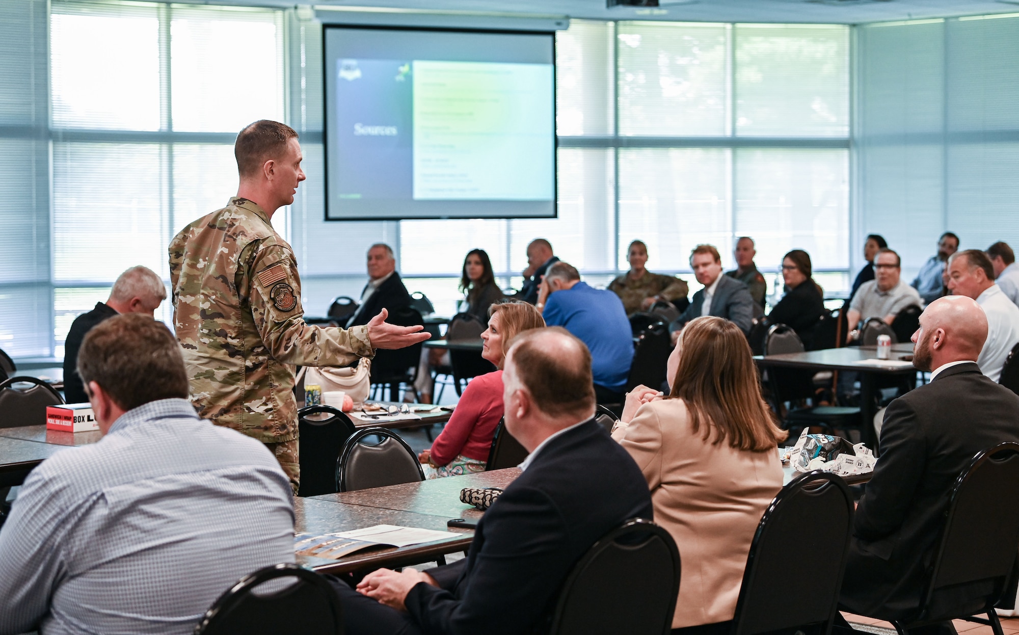 A uniformed airman addresses a crowd of local civilian leaders.