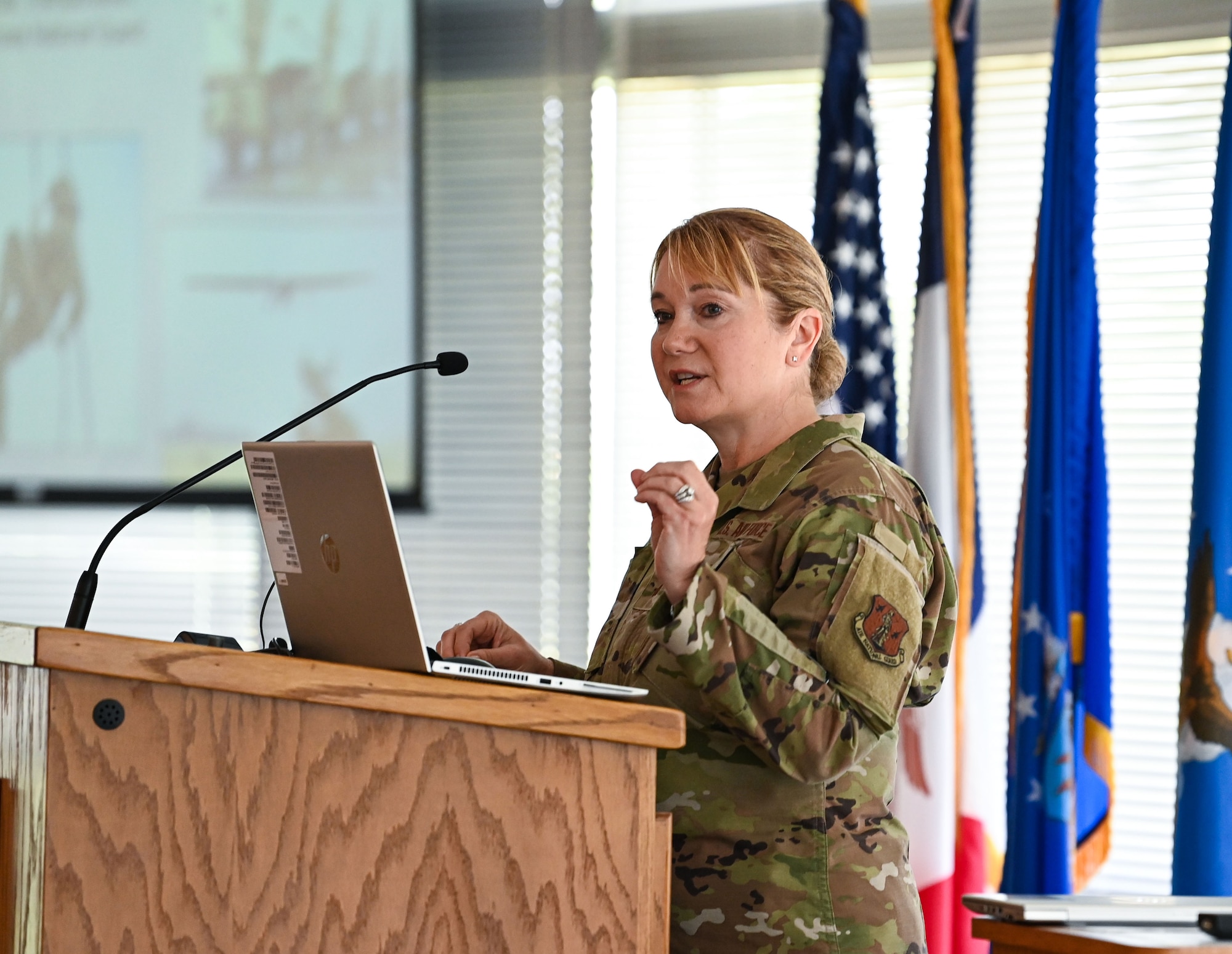 Female general in camo uniform stands behind podium speaking