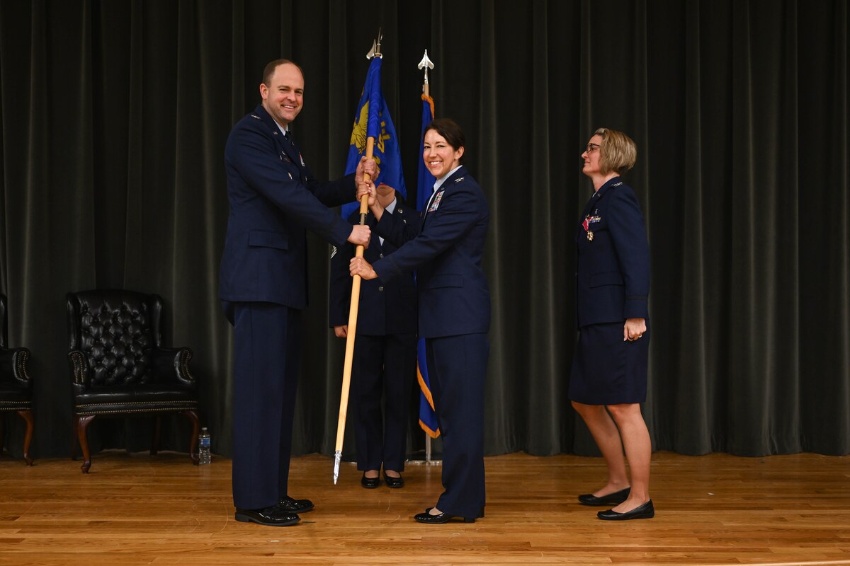 Four military members on stage and one passes a flag to the other.