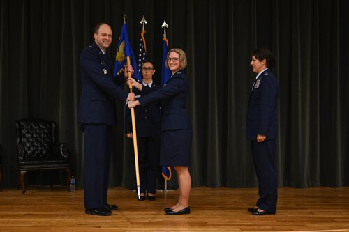 Four military members on stage and one passes a flag to the other.