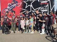 riders, kids and adults in front of the BMX Pro Stunt trailer looking at the camera.