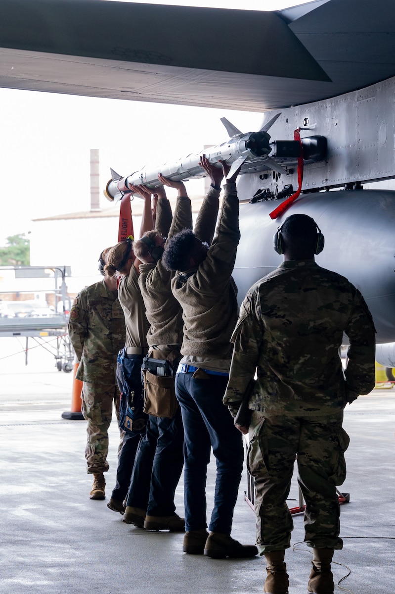 492nd FGS weapons load crew members place a munition onto an F-15E Strike Eagle together during a load crew competition