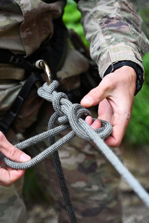 A soldier ties a rope to his or her harness in preparation for a climb.