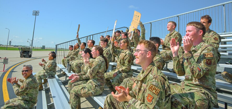 Airmen cheer from the stands for their team during the 5th Maintenance Group’s inaugural Mission Generation Competition at Minot Air Force Base, North Dakota, July 17, 2024. The competition consisted of changing a jet tire, assembling guided munitions, and attaching munitions to a B-52H Stratofortress.