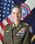 Female Army Soldier in uniform with medals smiles while posed in front of both the U.S. and the Army Recruiting Brigade flags