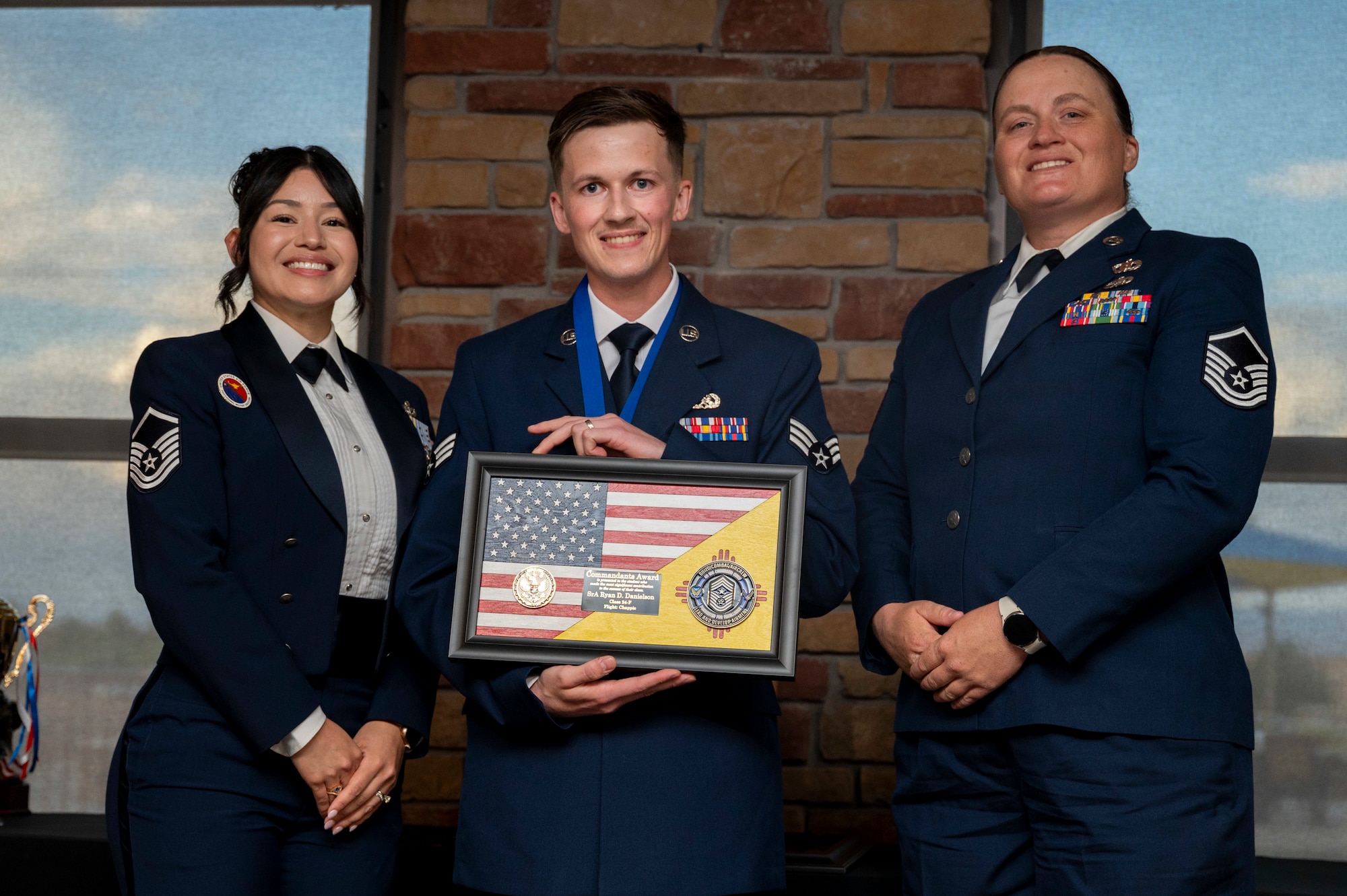 U.S. Air Force Senior Airman Ryan Danielson, Airman Leadership School Graduate, center, accepts the Commandant’s Award from U.S. Air Force Master Sgt. Cecilia Ayon, left, and U.S. Air Force Master Sgt. Angela McAllister, during the graduation of Joel C. Mayo ALS Class 24-F at Holloman Air Force Base, New Mexico, July 18, 2024.