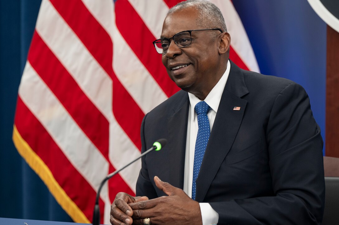 Secretary of State Lloyd J. Austin III speaks into a microphone on a podium with the American flag behind him.