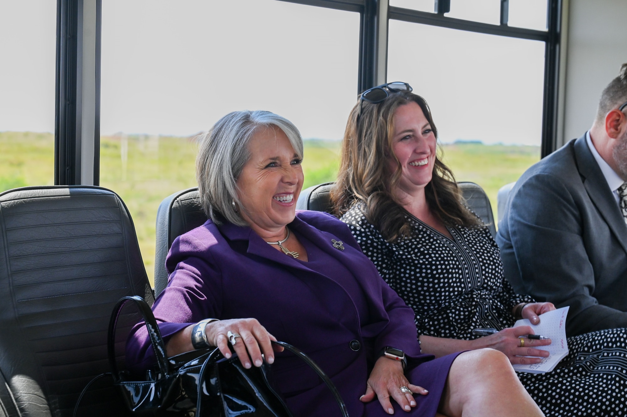 Two women in business attire sit inside a vehicle smiling and laughing.