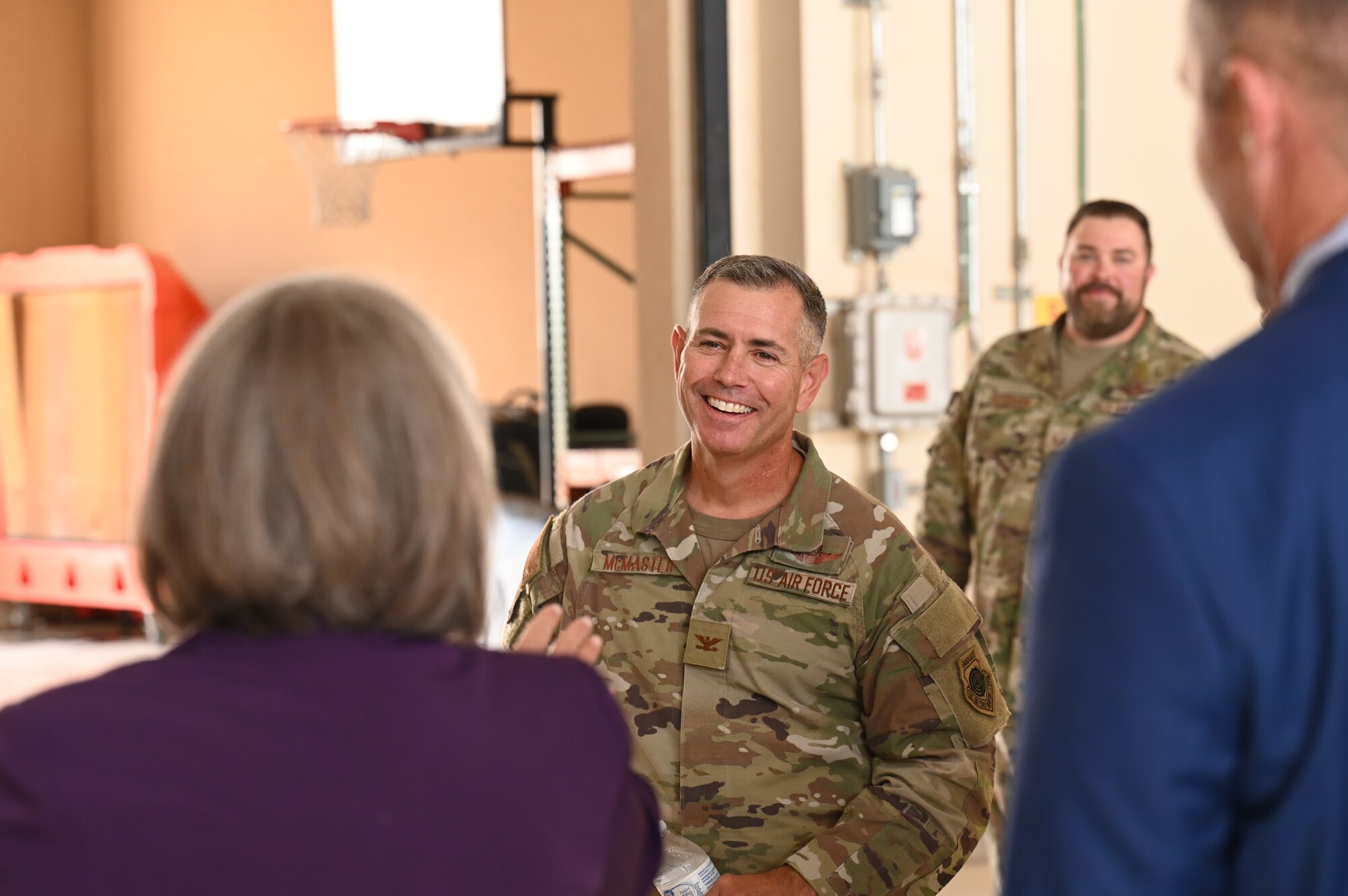 A man in military uniform smiles at a woman talking to her.