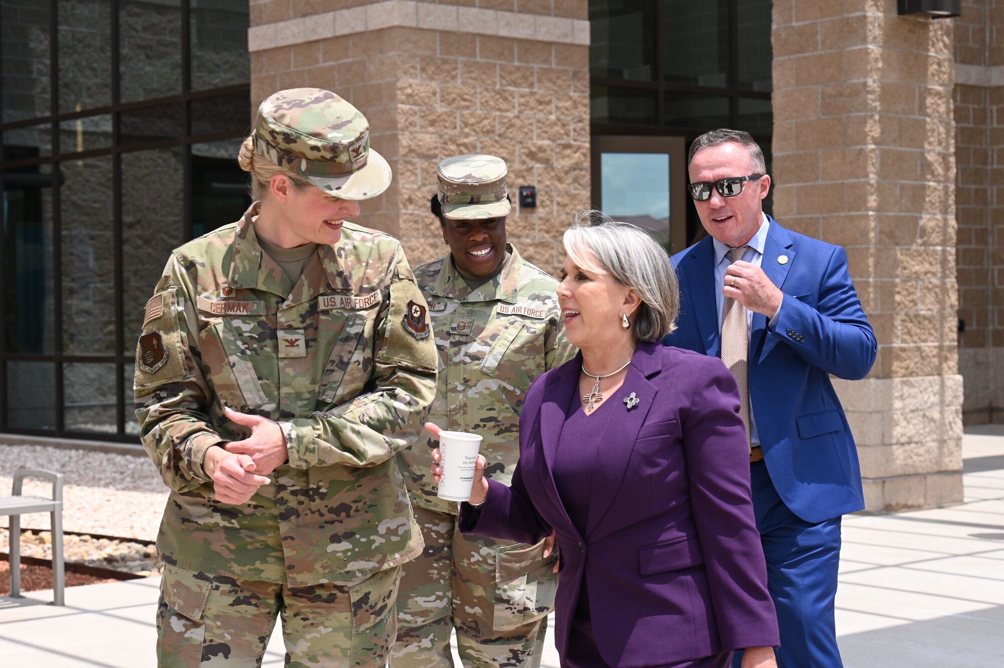 A woman holding a cup walks with a man, and two women in military uniform.