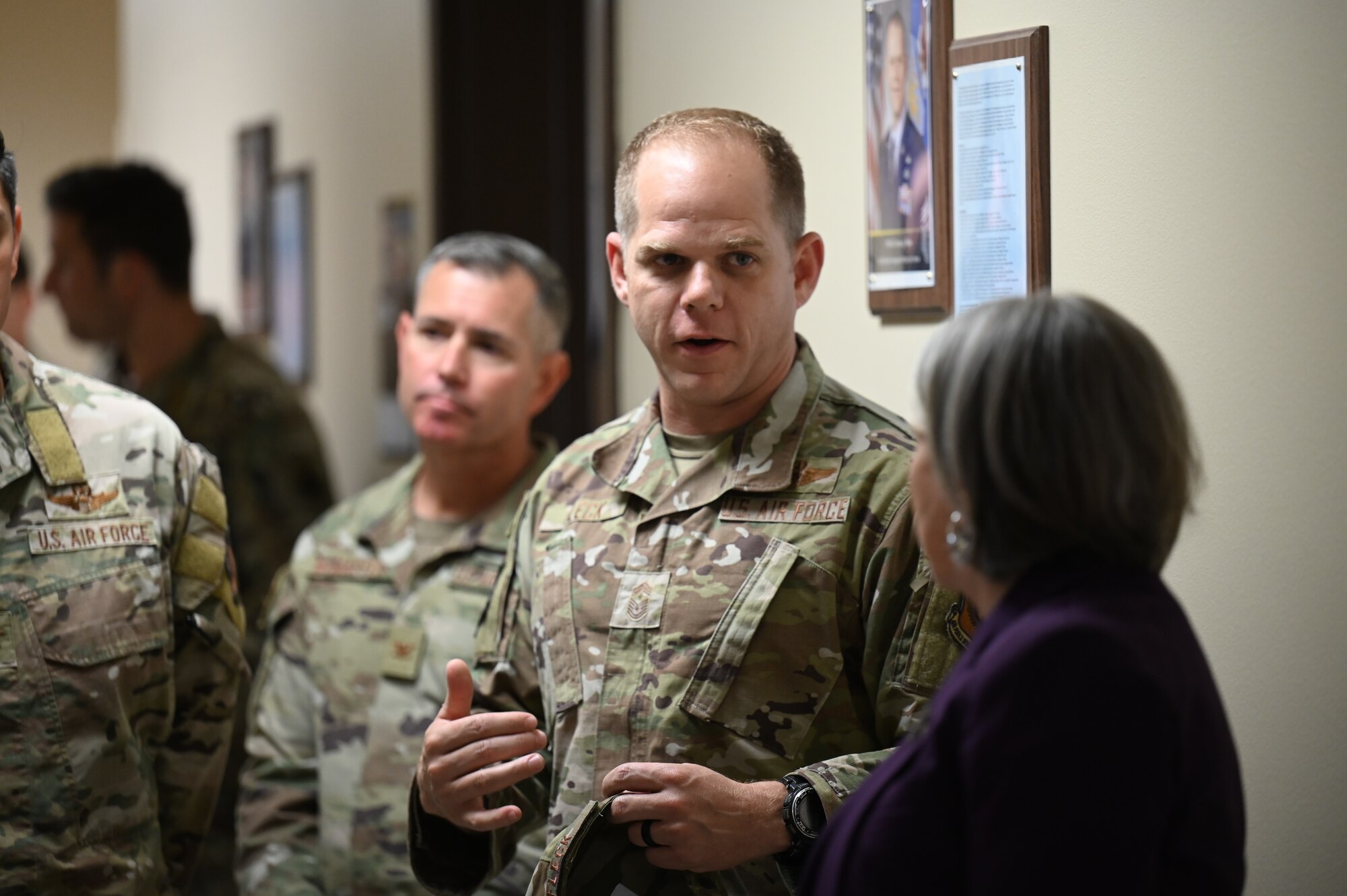 A man in military uniform converses with a woman in a hallway.