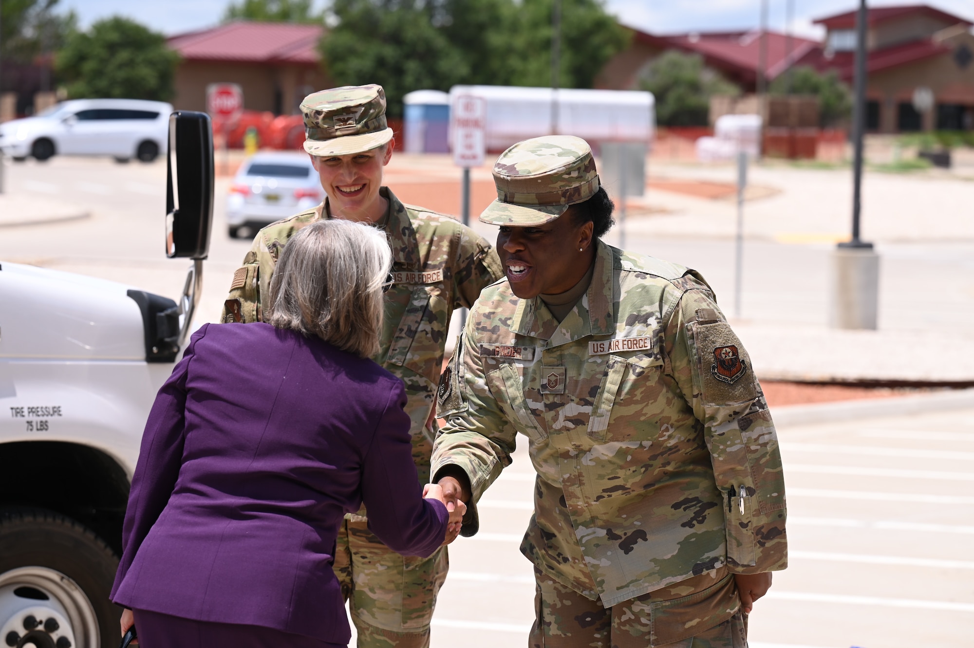 A woman shakes hands with another woman in military uniform, with a third woman in uniform standing by.
