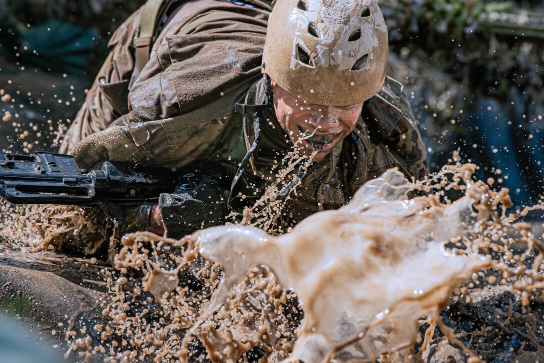 An Air Force basic cadet trainee crawls through the mud while carrying a weapon.