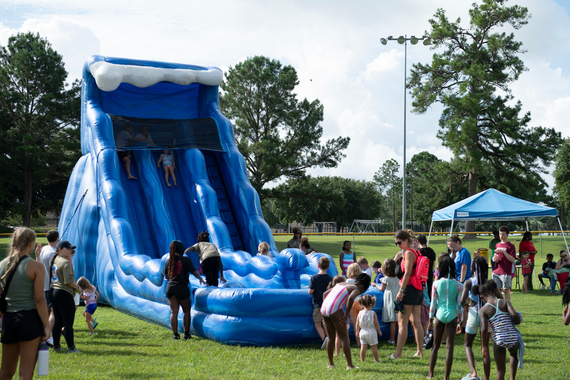 A water slide sits in a field with children and adults standing around or going down the slide.