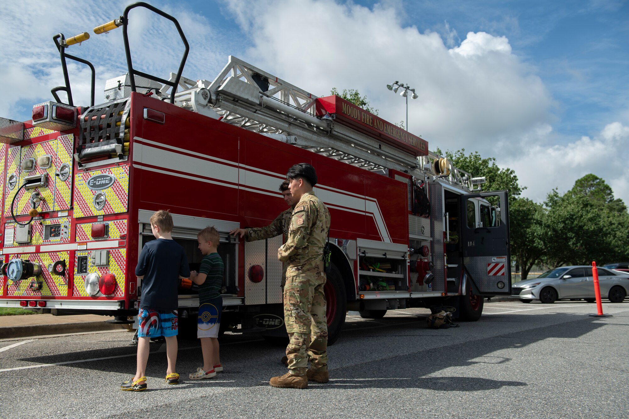 Two adult military members and two children standing next to a firetruck.