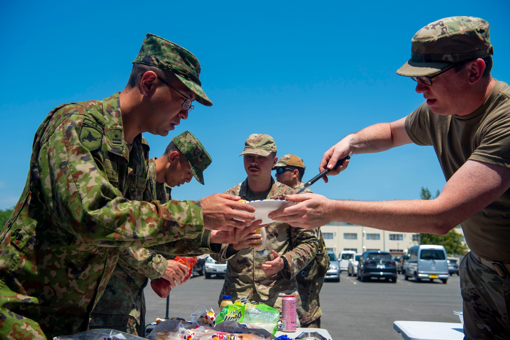 U.S. Air Force Tech. Erwin Armstrong III, right, 35th Communications Squadron section chief, places a hamburger on Japan Ground Self-Defense Force Maj. Makoto Nakamura, Basic English Training course instructor, plate during a JGSDF Basic English Training Course tour at Misawa Air Base, Japan, July 18, 2024.