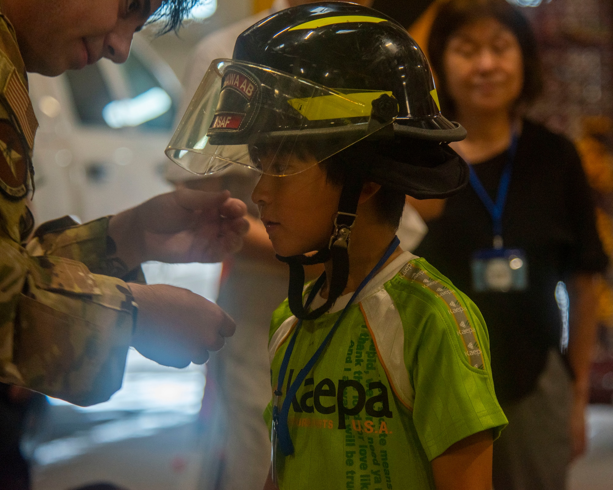 U.S. Air Force Senior Airman Preston Holladay, left, 35th Civil Engineer Squadron noncommissioned officer in charge of dispatch, places a firefighter helmet on a Misawa Friendship Tour participant at Misawa Air Base, Japan, July 19, 2024.