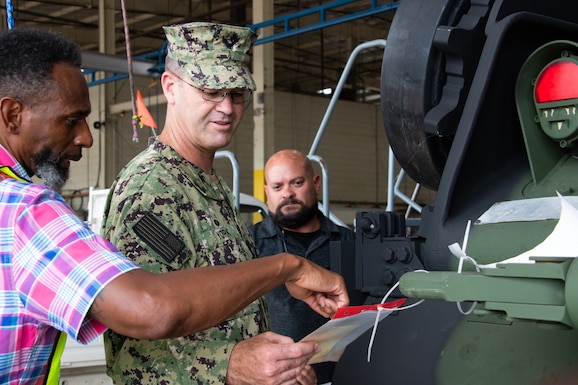 A man in U.S. Navy camouflage inspects a tag hanging from a piece of U.S. Army equipment