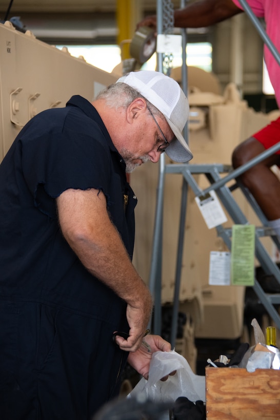 A man in a white hat cuts shipping plastic.