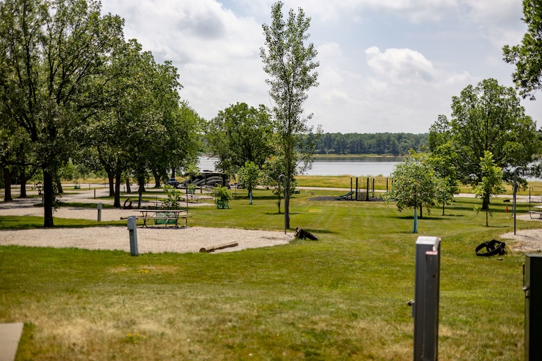 Green grass with a concrete pad in the middle, trees to the left, and water in the background.