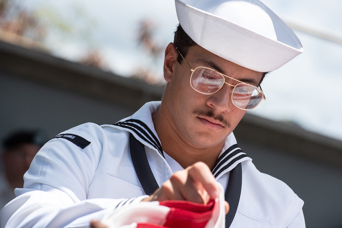 Close-up of a sailor wearing glasses and looking down to fold a flag.