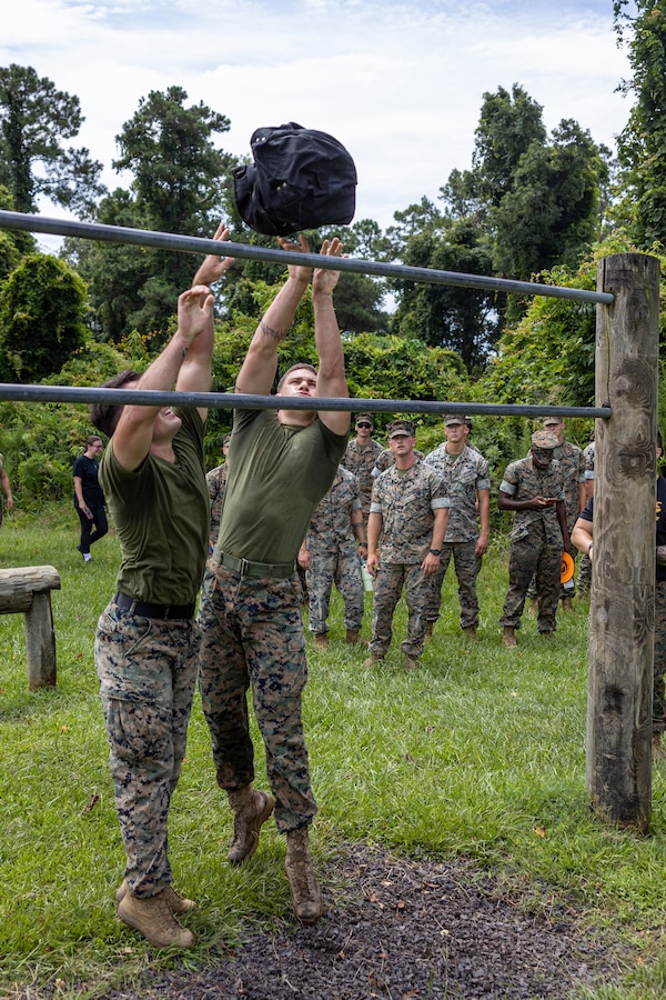 U.S. Marines with 2nd Marine Logistics Group throw weighted sandbags over the double bar section of an obstacle course during the Fittest of the 2nd MLG event hosted by the 2nd MLG Human Performance Center on Camp Lejeune, North Carolina, July 19, 2024. Teams from across 2nd MLG regiments and battalions competed for the title of “Fittest of 2nd MLG” in order to promote physical fitness, camaraderie, and friendly competition. (U.S. Marine Corps photo by Lance Cpl. Christian Salazar)