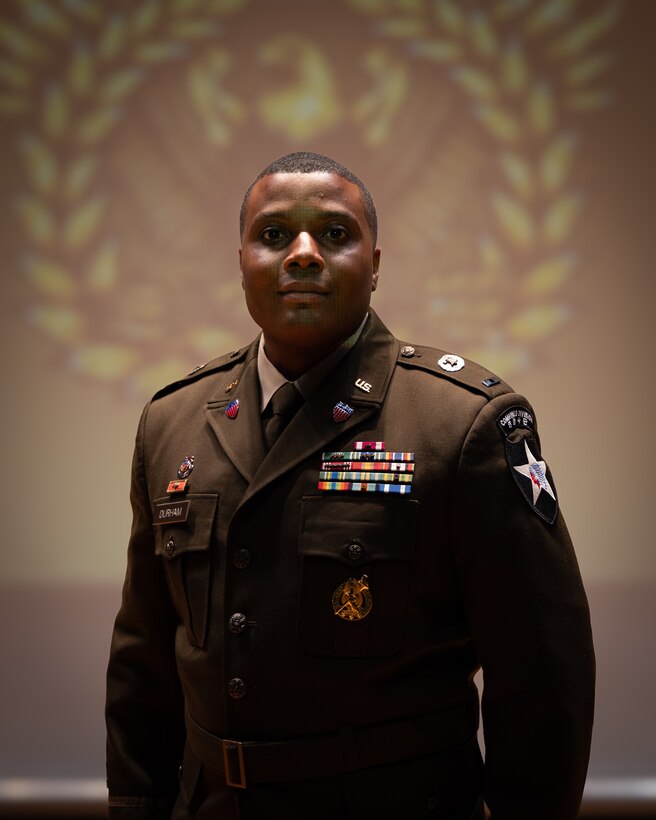 man wearing U.S. Army uniform stands on a stage.