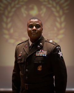 man wearing U.S. Army uniform stands on a stage.