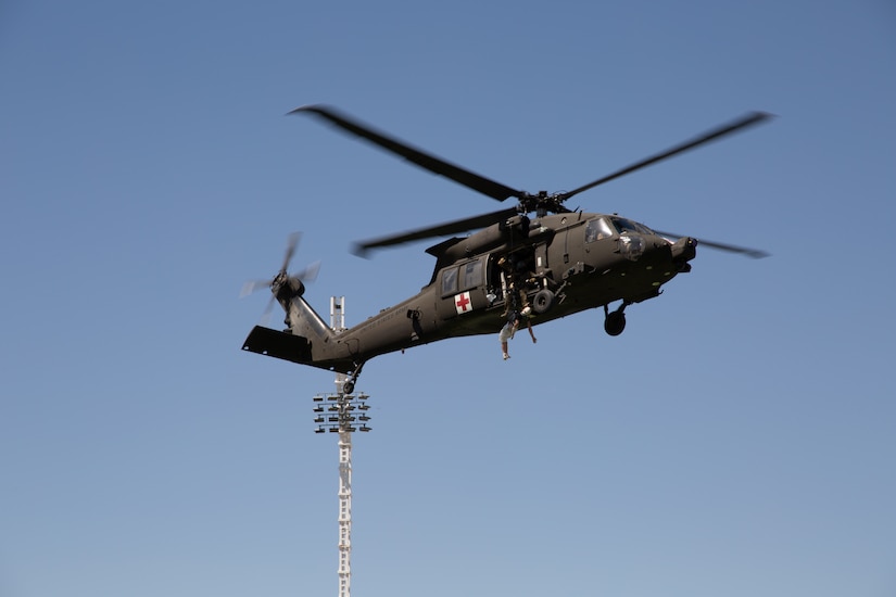 A uniformed service member jumps out of a moving military helicopter.