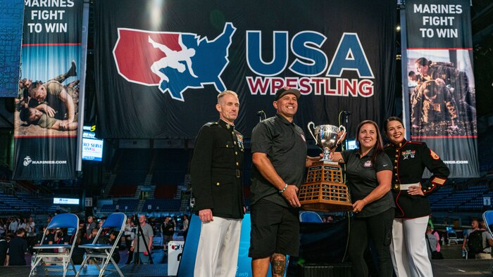 U.S. Marine Corps Col. Joseph Galvin, commanding officer of Headquarters and Service Battalion, Marine Corps Installation East, Marine Corps Base Camp Lejeune, left, and Staff Sgt. Courtney Glen White, communication strategy and operations chief with 12th Marine Corps District, present the national team title to the coaches of Team California at the 2024 U.S. Marine Corps Junior & 16U Nationals in Fargo, North Dakota, July 14, 2024. The Marine Corps’ partnership with USA Wrestling started in 2017 as a way for Marines to develop new relationships with wrestling coaches. These partnerships ensure the coaches of the next generation of Marines are aware of Marine Corps opportunities, provide advocacy and support recruiter access to prospective audiences, which is critical to our nation's defense. (U.S. Marine Corps photo by Sgt. Jesse K. Carter-Powell)