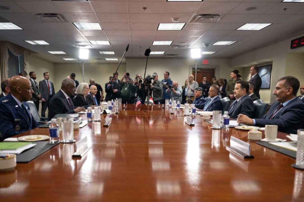 People in military and civilian attire sit around a large conference table.