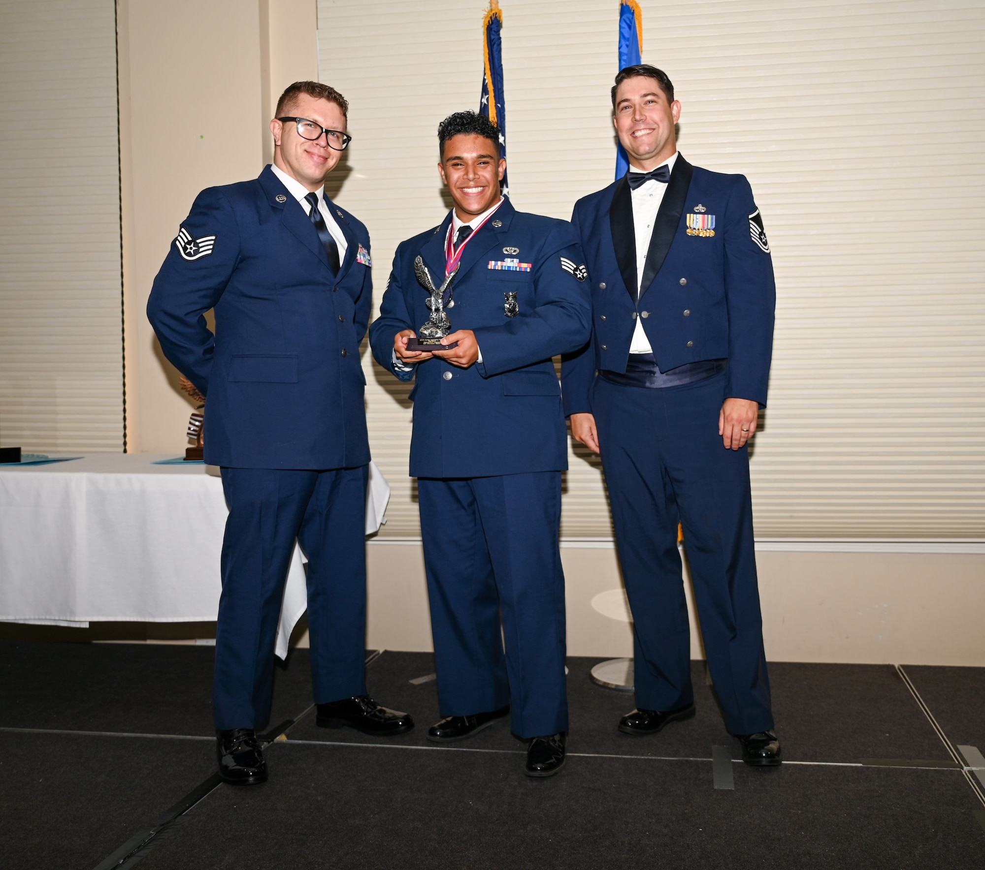 U.S. Air Force Senior Airman Marwane Hsaini, 4th Civil Engineer Squadron fire crew chief, center, accepts the Distinguished Graduate Award from Staff Sgt. Joshua Irwin, left, 4th Operations Support Squadron wing scheduling non-commissioned officer in charge, and Master Sgt. Nicolas Lamonica, 335th Fighter Generation Squadron specialist section chief, during the ALS class 24-E graduation ceremony at Seymour Johnson Air Force Base, North Carolina, June 27, 2024. Students awarded the Distinguished Graduate Award displayed effective teamwork, academic excellence and leadership skills. (U.S. Air Force photo by Airman Rebecca Tierney)