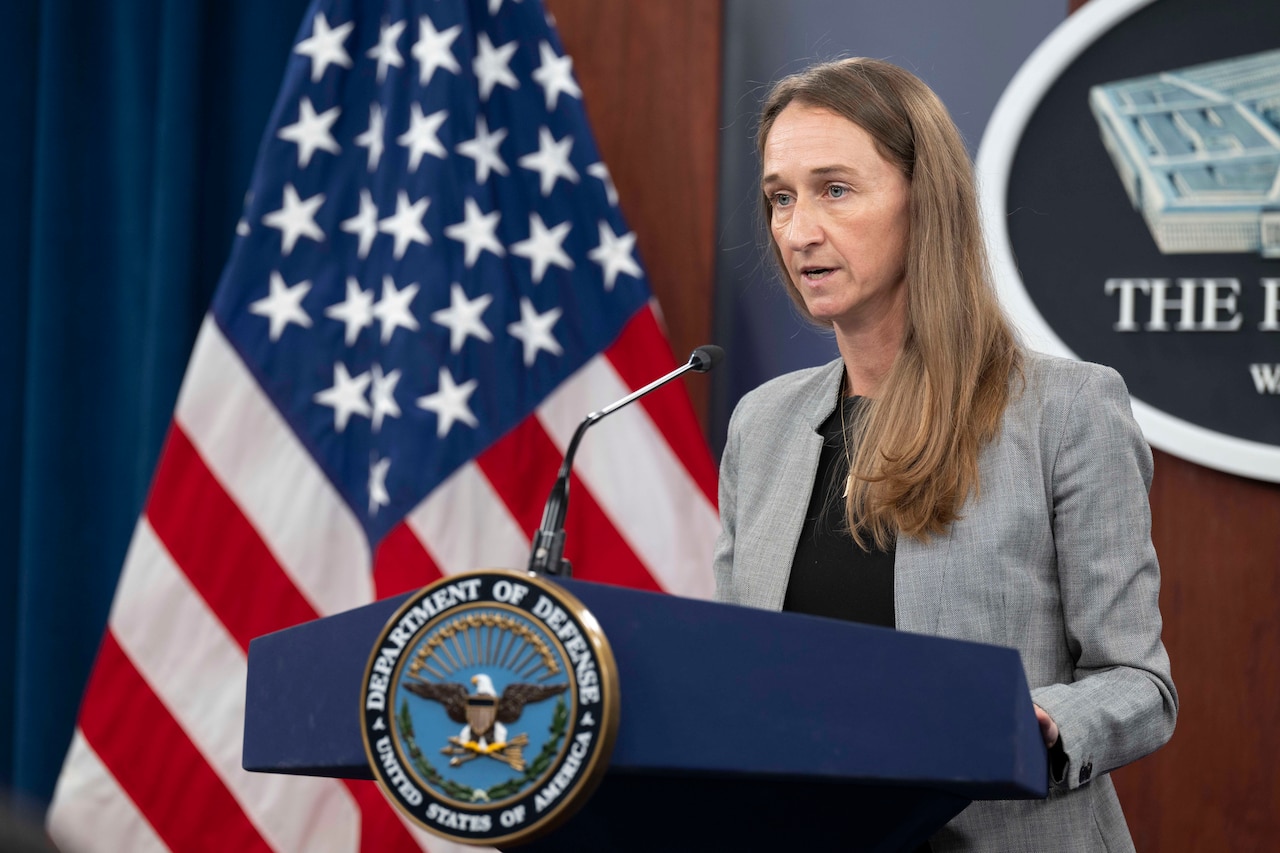 A civilian speaks at a lectern with the American flag and the Pentagon seal in the background.
