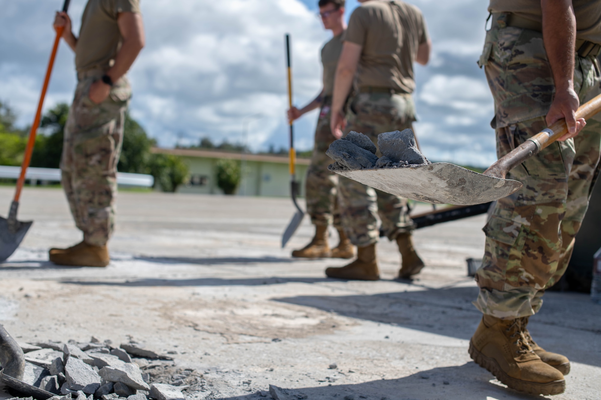 military members holding shovels move broken concrete