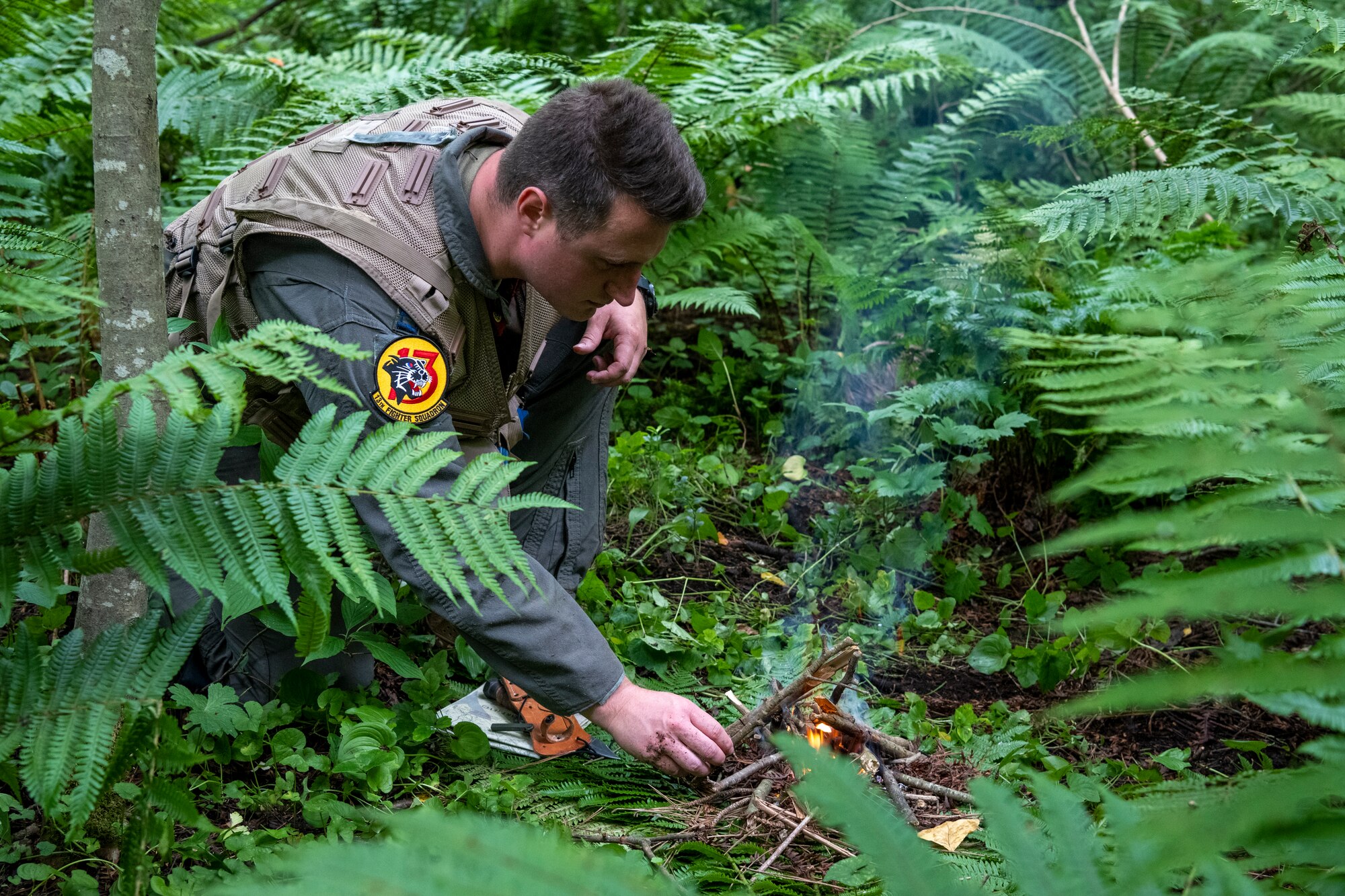 U.S. Air Force Capt. Charles Trader, 13th Fighter Squadron pilot, places branches on a fire during a Combat Survival Training exercise led by Survival, Evasion, Resistance, Escape (SERE) specialists at Draughon Range near Misawa Air Base, Japan, July 16, 2024.